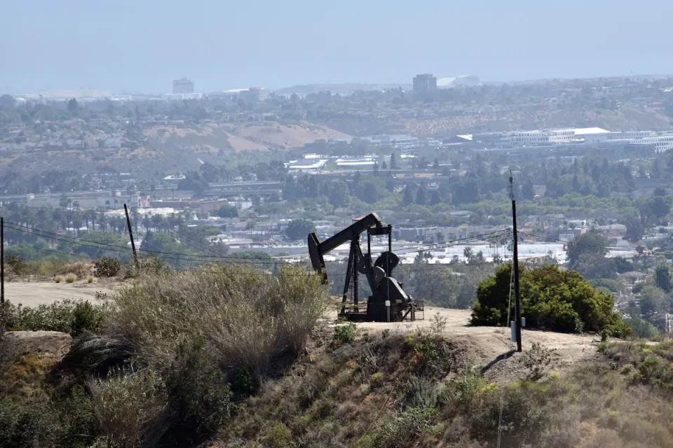 Oil well on hilltop in Los Angeles with city neighborhoods in background.